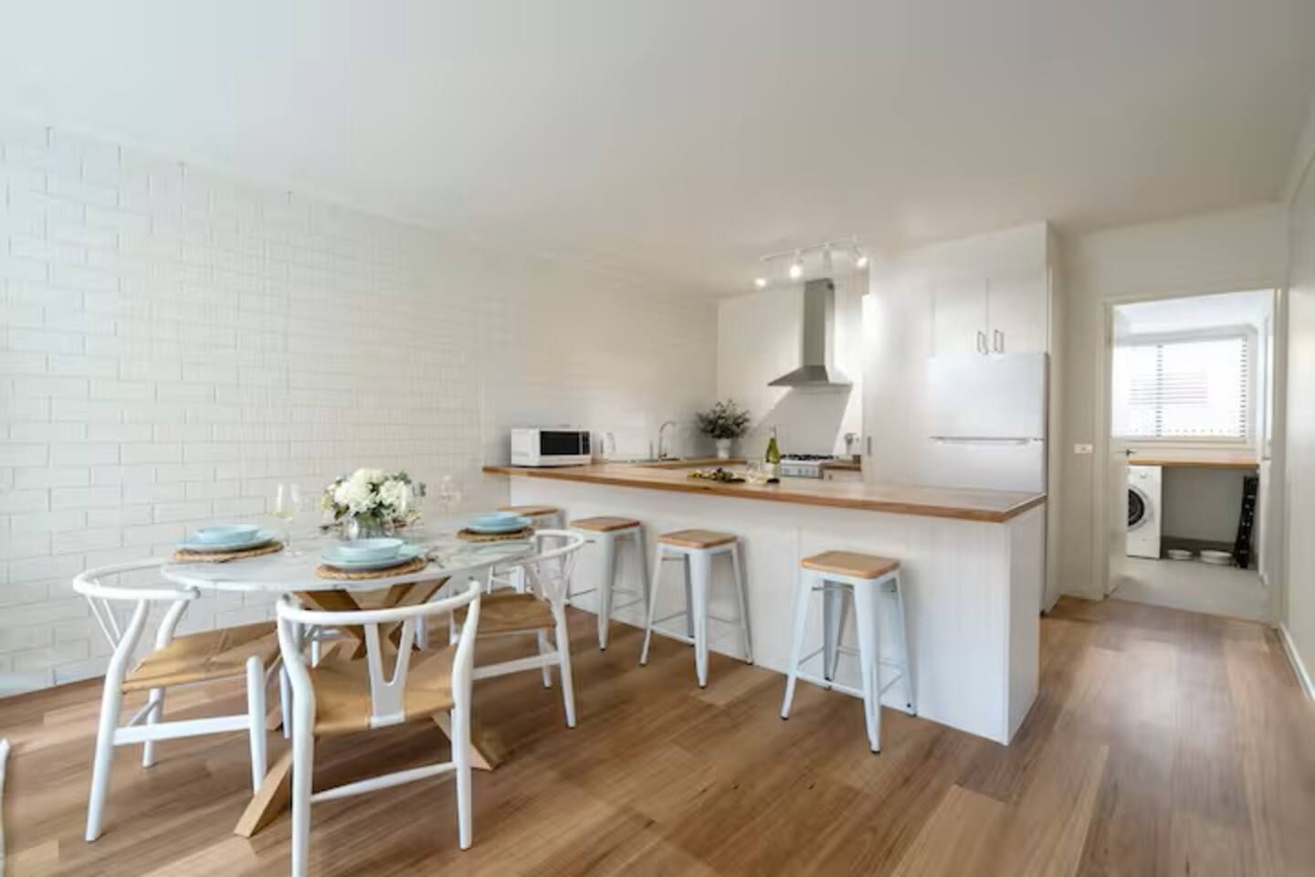 A modern kitchen with a dining area, white appliances, and a wooden floor.
