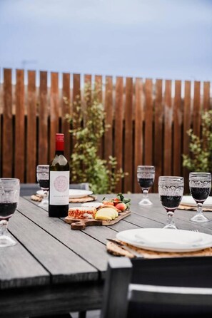 A wooden table set for a meal with a bottle of wine, glasses, and a cheese board. - River Grove Retreat | 100m to River | Pet Friendly (Ocean Grove)