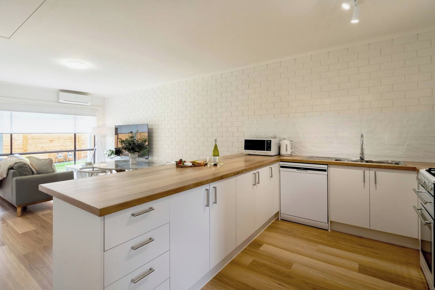 A modern kitchen with white cabinetry, a wooden countertop, and a built-in dishwasher.