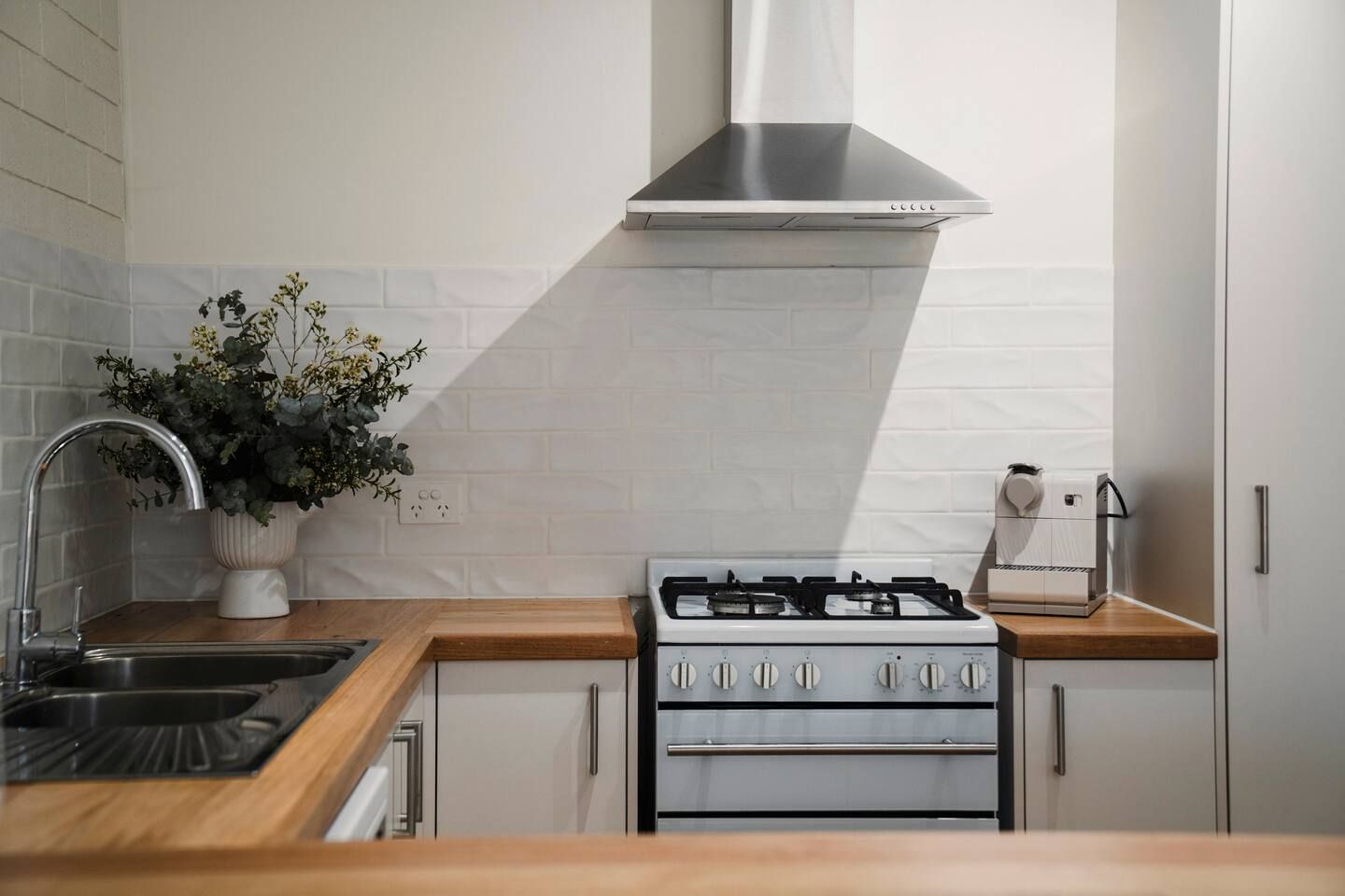 A kitchen with a stainless steel range hood, a sink with a faucet, a stove, and a potted plant.