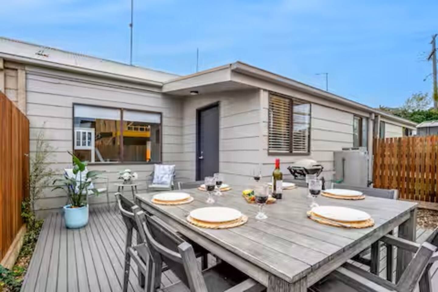 A wooden deck with a dining table set for six, surrounded by chairs.