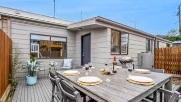A wooden deck with a dining table set for six, surrounded by chairs.