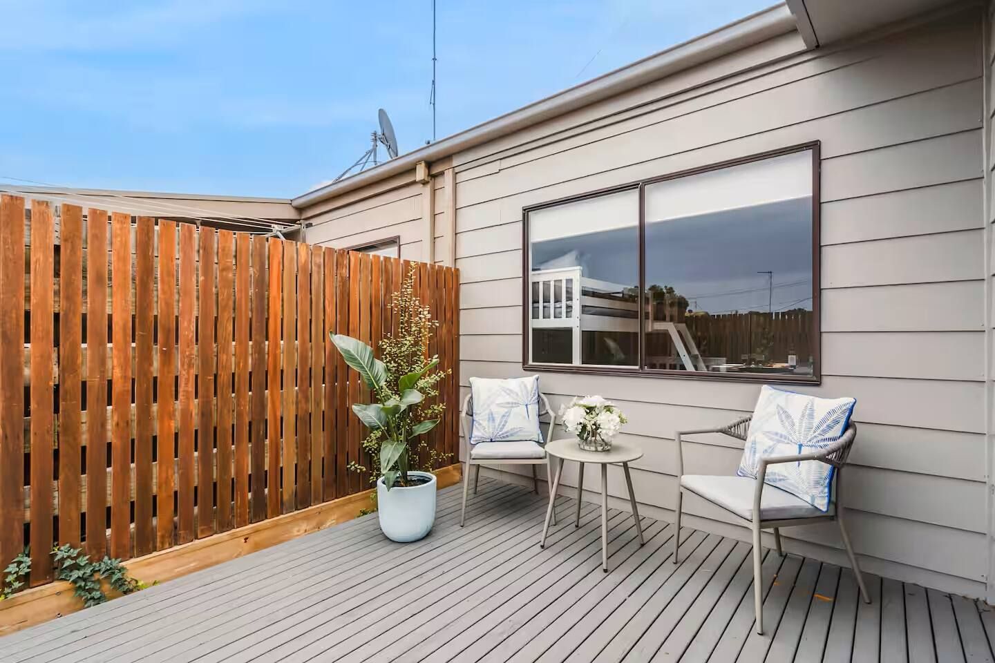 A deck with two chairs and a table, a wooden fence, and a large window.
