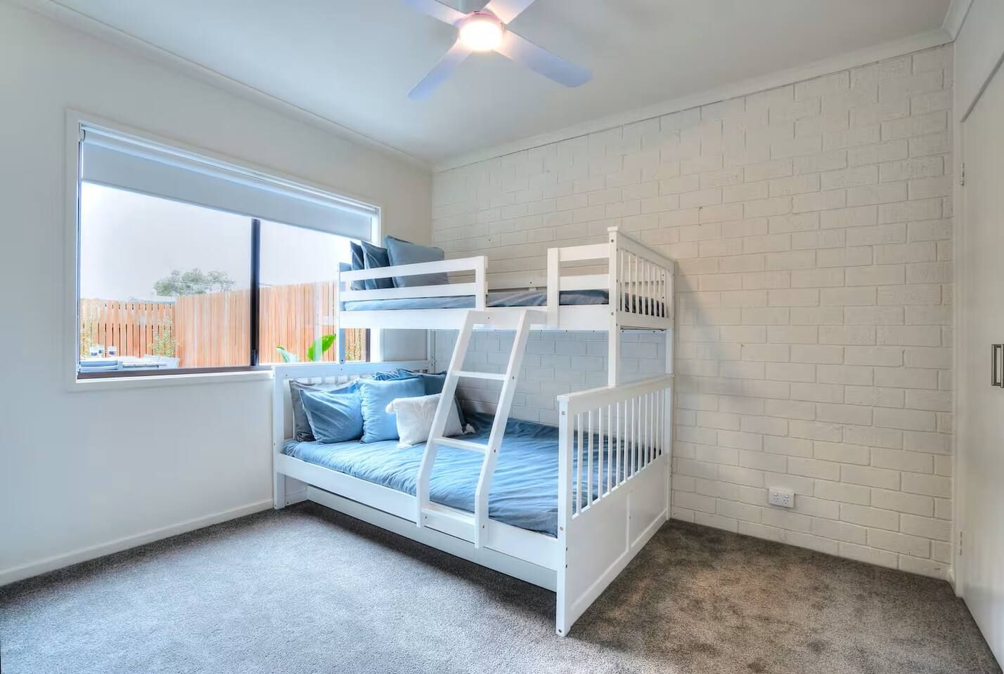 A bunk bed room with a window, white brick walls, and a ceiling fan.