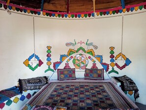 Een kamer met een bed, een muur met kleurrijke patronen en een plafond met een decoratieve lijst.