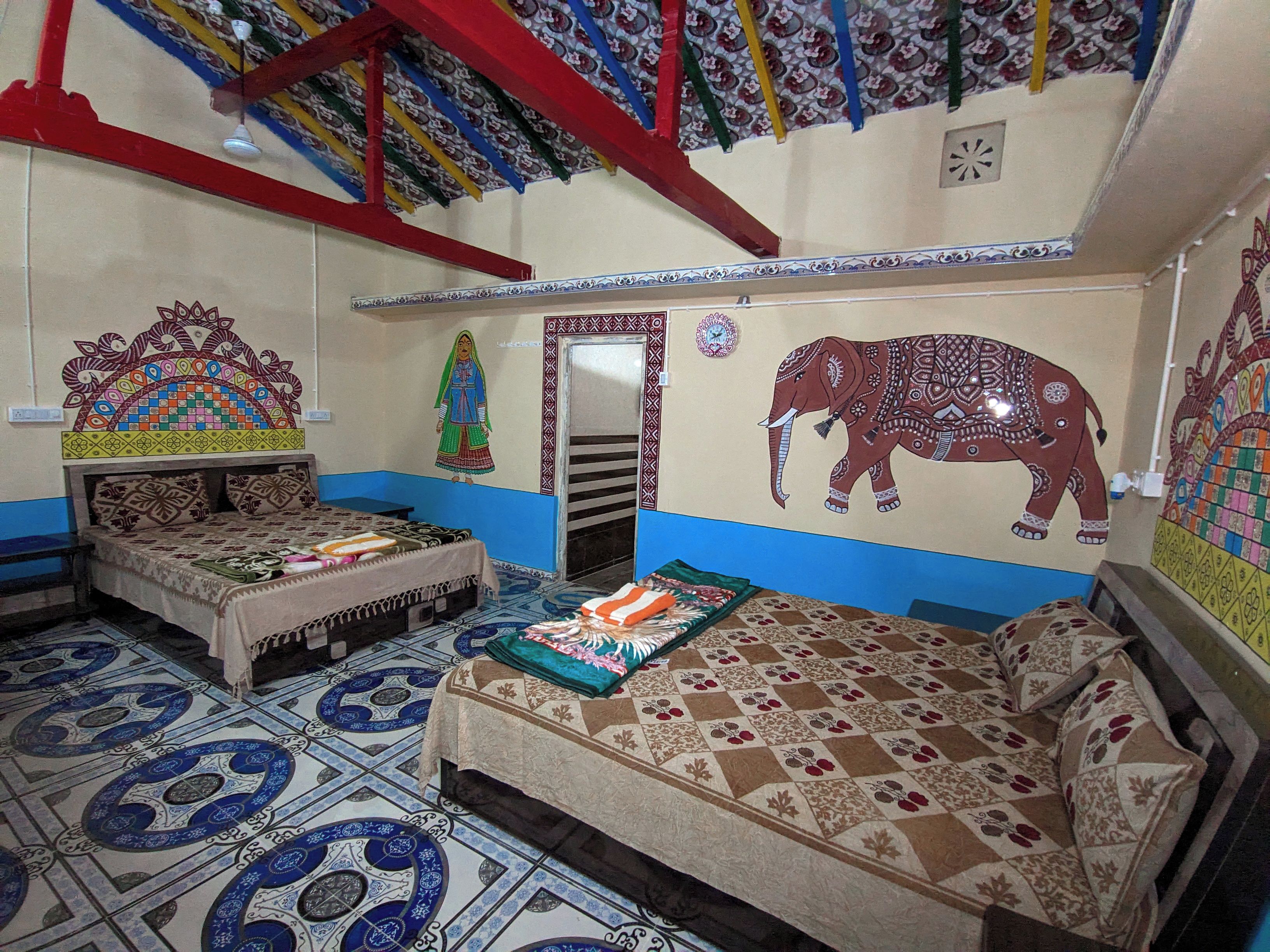 Una habitación con dos camas, un mural de un elefante en la pared y un suelo estampado.