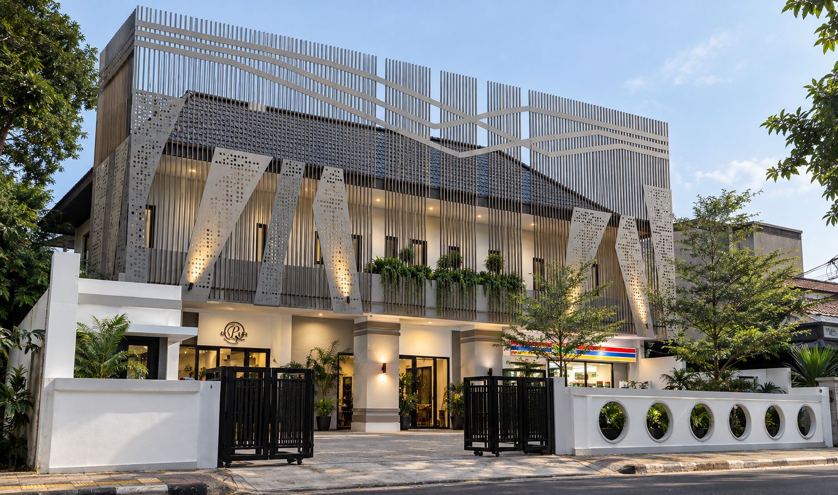 Ein modernes Hotel mit einer markanten Fassade aus vertikalen Lamellen und perforierten Paneelen, einem verschlossenen Eingangsbereich und einem gepflegten Außenbereich mit Topfpflanzen.