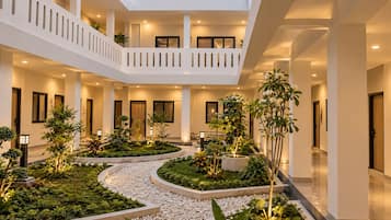 Ein mehrgeschossiges Atrium mit einem zentralen Garten, Balkonen und einer Reihe von Türen zu Zimmern.