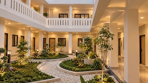 A multi-level atrium with a central garden, balconies, and a series of doors leading to rooms.