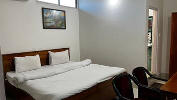 A bedroom with a bed, two chairs, a desk, and a painting on the wall.