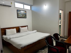 Un dormitorio con una cama, dos sillas, un escritorio y un cuadro en la pared.