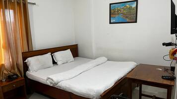 A single bed with white bedding, a wooden headboard, a bedside table with a telephone, and a painting on the wall.