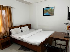 A single bed with white bedding, a wooden headboard, a bedside table with a telephone, and a painting on the wall.
