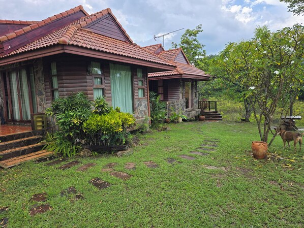 A wooden house with a tiled roof, a stone foundation, and a grassy yard with stepping stones.