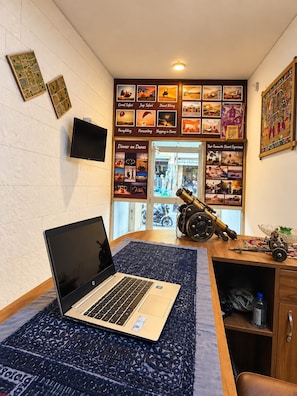 A room with a laptop on a patterned rug, a telescope, and a wall decorated with desert-themed pictures. - Hotel Alexa Palace (Jaisalmer)