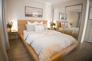 A modern bedroom with a large bed, bedside tables, a mirror, and a painting on the wall. - Peaceful Cottage Conveniently Located (Shailer Park)