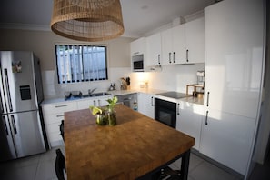 A modern kitchen with white cabinets, a wooden table, and a hanging light fixture. - Peaceful Cottage Conveniently Located (Shailer Park)