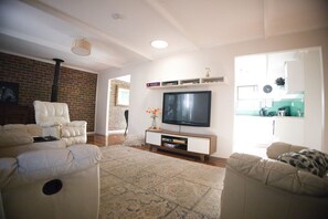 Een woonkamer met een flatscreen televisie, twee banken, een salontafel en een vloerkleed met een patroon.