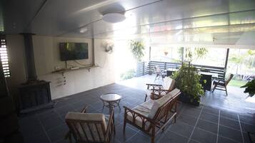 A covered patio area with a seating arrangement, a television mounted on the wall, and a view of the outdoors.