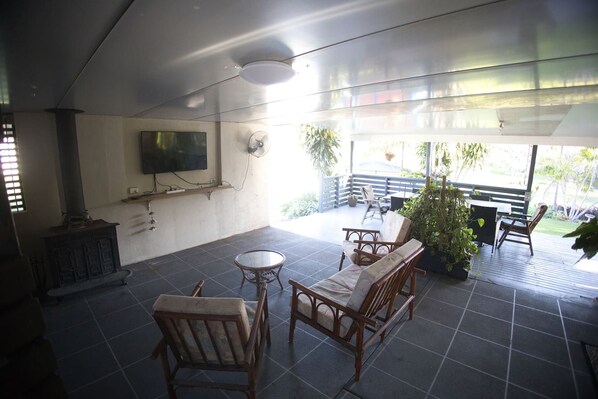 Een overdekt terras met een zithoek, een aan de muur bevestigde televisie en uitzicht op de omgeving.