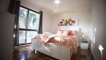 A bedroom with a bed, a nightstand, a ceiling fan, a window with curtains, and a painting on the wall.