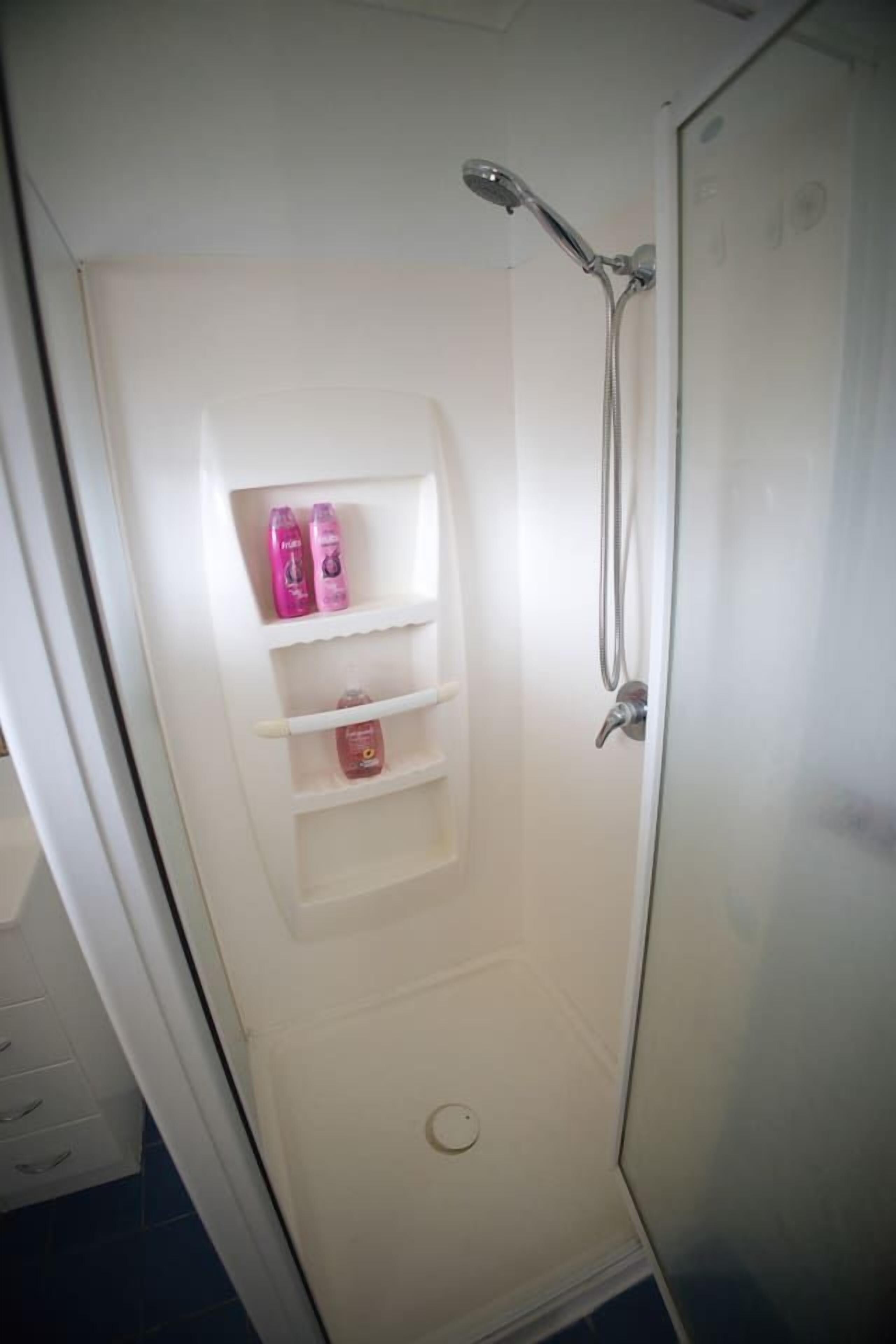 A shower with a glass door, a shelf with toiletries, and a showerhead.