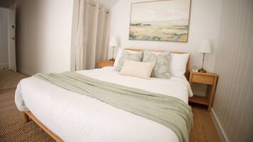Quarto com cama, duas mesas de cabeceira, luminária, quadro na parede e porta.