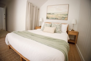 A bedroom with a bed, two bedside tables, a lamp, a painting on the wall, and a door. - Private-Pool Studio in Currumbin (Currumbin)