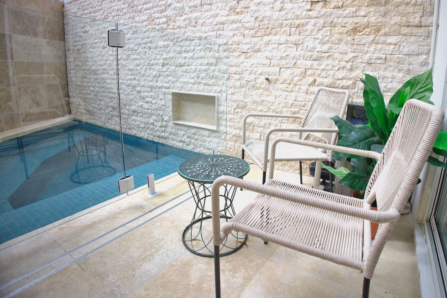 An indoor swimming pool with a stone wall backdrop, a round table, and wicker chairs.