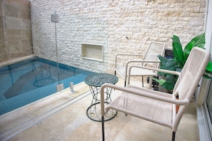 An indoor swimming pool with a stone wall backdrop, a round table, and wicker chairs. - Private-Pool Studio in Currumbin (Currumbin)
