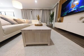 Un salon moderne avec un canapé de couleur claire, une table basse en bois et un téléviseur à écran plat fixé au mur.