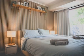 A bedroom with a bed, bedside lamps, a nightstand, a window with curtains, and a wall-mounted shelf with decorative items. - Convenient and Tranquil Retreat in Brisbane South (Shailer Park)