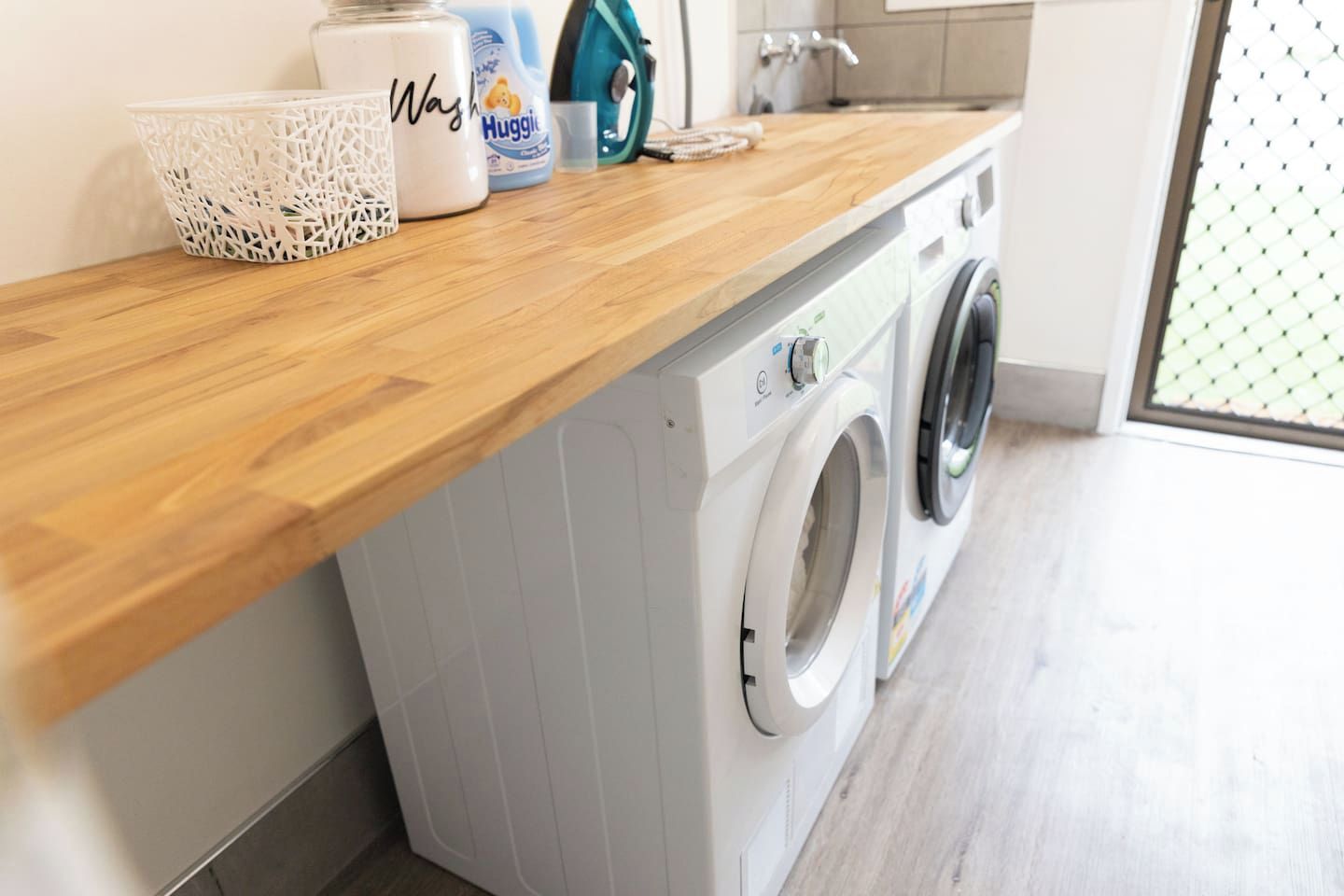 A laundry area with a washing machine, a basket, and a container of detergent.