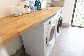 A laundry area with a washing machine, a basket, and a container of detergent. - Convenient and Peaceful Studio in Brisbane South (Shailer Park)