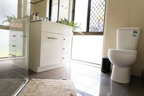 Un baño moderno con inodoro blanco, cabina de ducha de vidrio y tocador blanco con lavamanos.