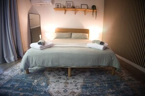 A bedroom with a bed, two bedside tables, a mirror, a wall-mounted shelf with decorative items, and a patterned rug. - Convenient and Peaceful Studio in Brisbane South (Shailer Park)