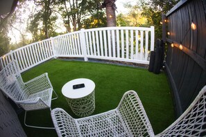 A fenced outdoor patio with artificial grass, white wicker furniture, and string lights.