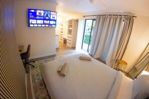 Una habitación de hotel con una cama, televisión montada en la pared, un escritorio y una ventana con cortinas.