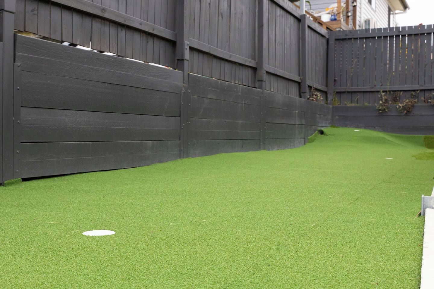 A fenced backyard with artificial green turf and a white circular object.