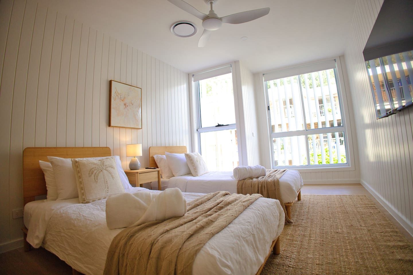 Un dormitorio con dos camas, ventilador de techo y ventanas amplias.