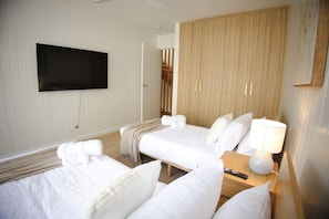 Une chambre d’hôtel avec deux lits, un téléviseur à écran plat fixé au mur, une armoire en bois et une table de chevet avec une lampe.