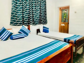 A room with two beds, each with a striped bedspread, a wooden headboard, and a white mattress. There is a door with a plant and a sign on it. - Green Haven Anuradhapura (Anuradhapura)