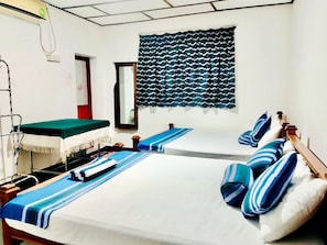 A room with two beds, a mirror, a window with patterned curtains, and a small table with a green tablecloth. - Green Haven Anuradhapura (Anuradhapura)