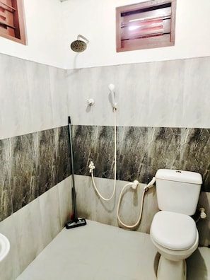 A bathroom with a toilet, a shower, and a mop. - Green Haven Anuradhapura (Anuradhapura)