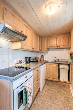A kitchen with wooden cabinets, a stove, a dishwasher, and a countertop with various appliances. - Bunloit Farmhouse by Interhome (Drumnadrochit)