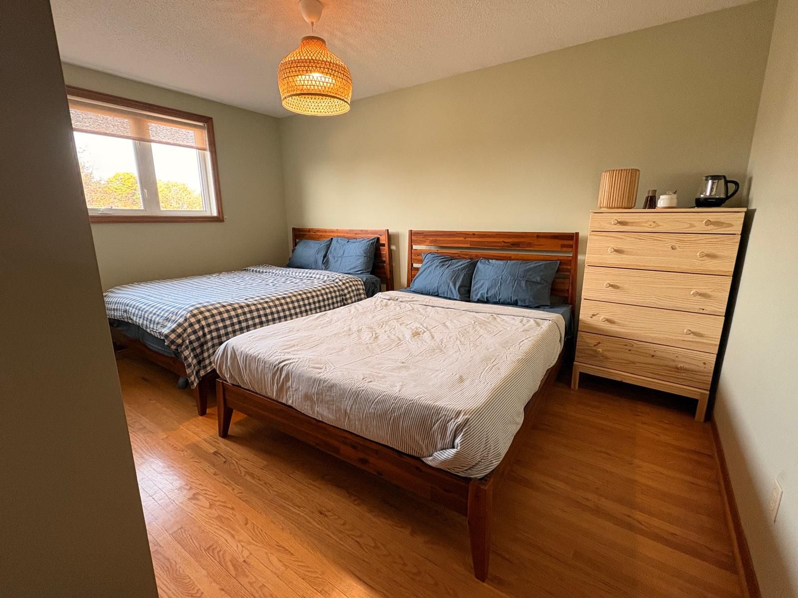 Une chambre à coucher avec deux lits en bois, une commode en bois et une fenêtre.