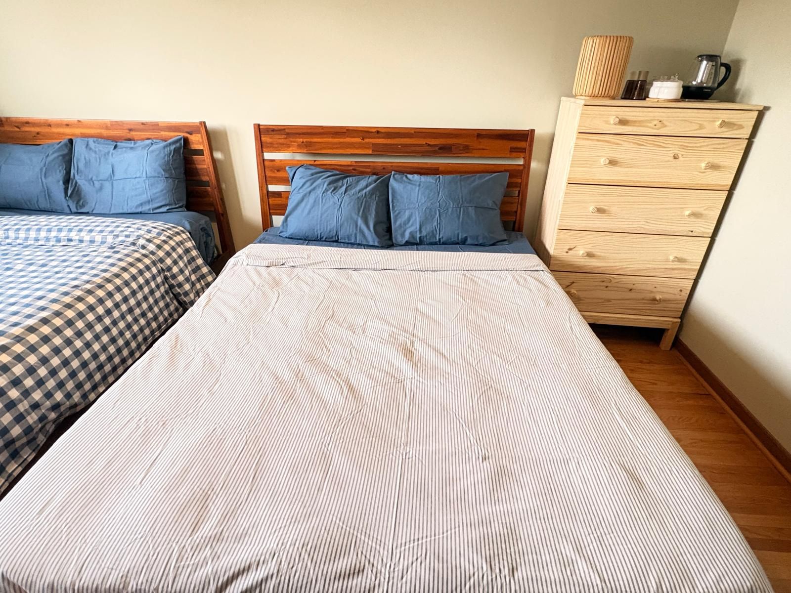 Une chambre avec deux lits, une tête de lit en bois, une commode et une bouilloire posée sur le dessus.