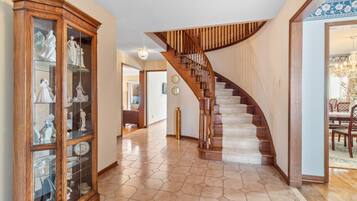A hallway with a wooden staircase, a glass cabinet with figurines, and a dining area with a table and chairs.