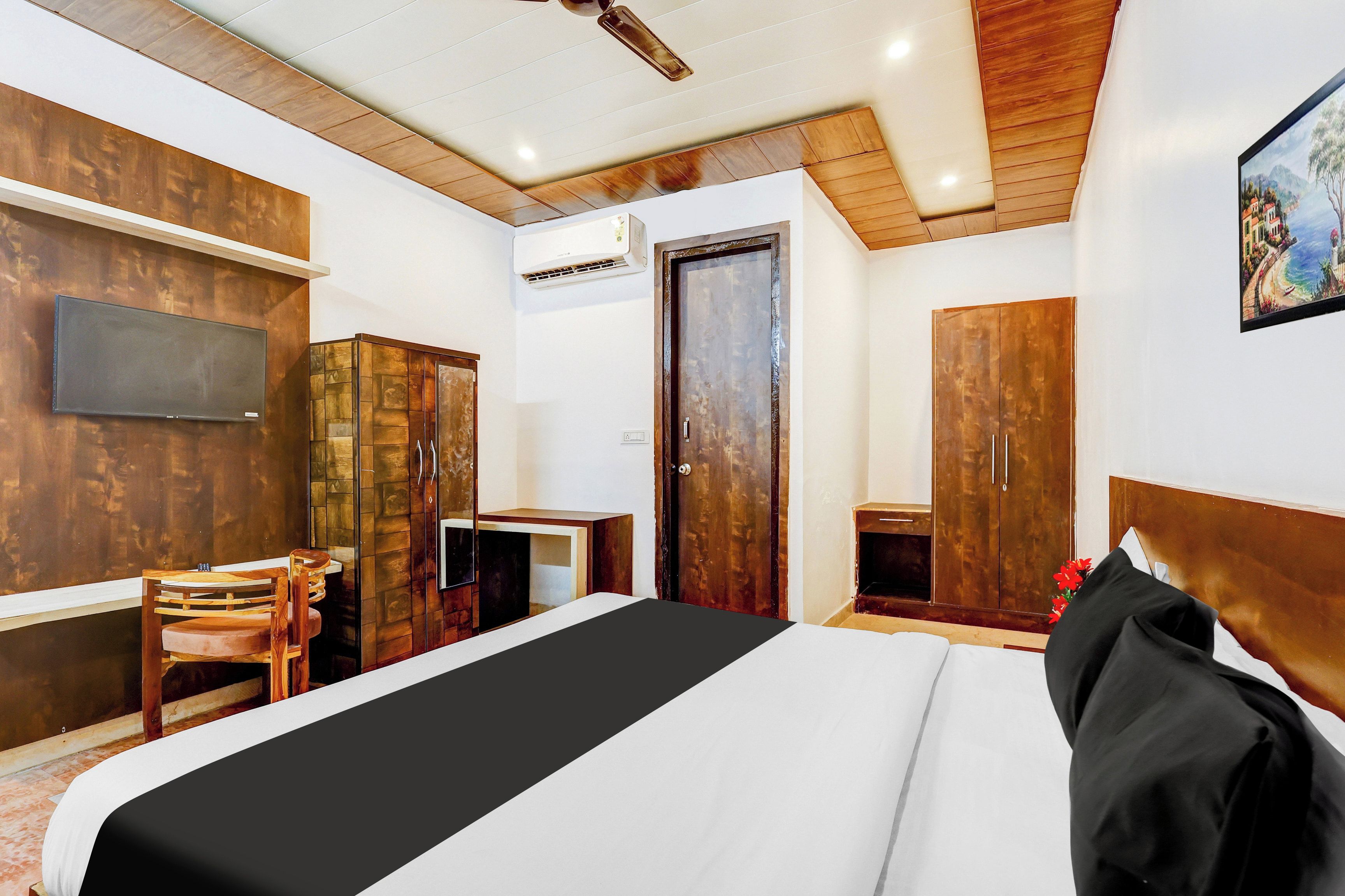 A hotel room with a bed, a desk, a chair, a wardrobe, and a television on the wall.