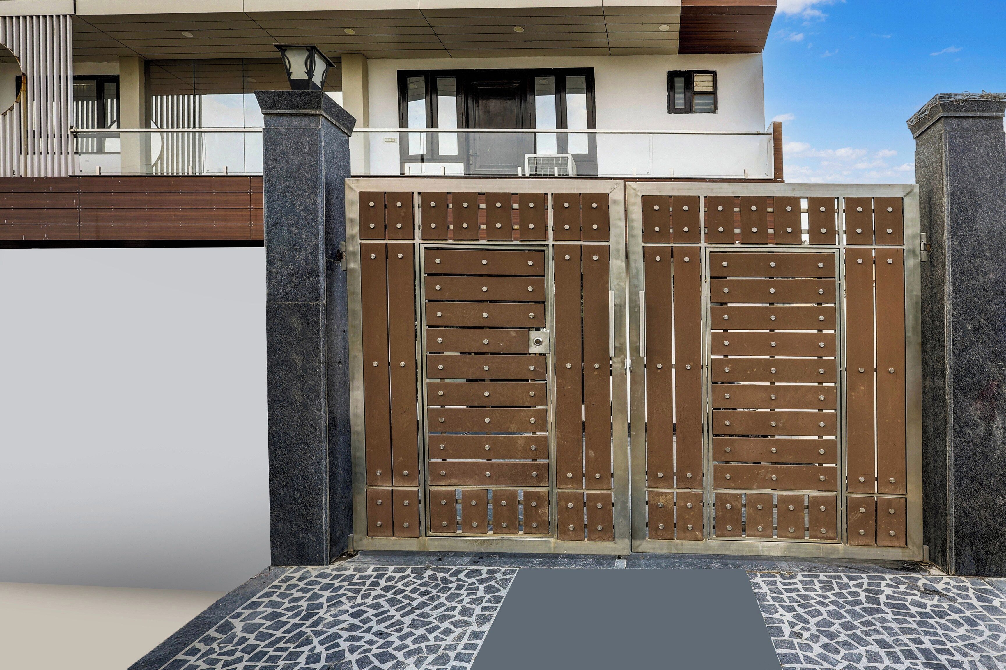 A gated entrance with a metal gate and a tiled pathway leading to a building with a balcony.
